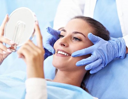 woman admiring her smile in hand mirror after cosmetic dental treatment 