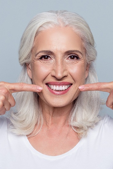 Older woman with dental implants pointing to her smile.