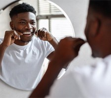 Man smiling at reflection while flossing his teeth