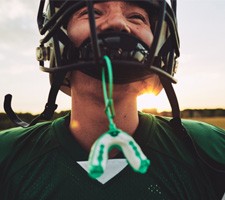 Green and white mouthguard hanging from football player's helmet