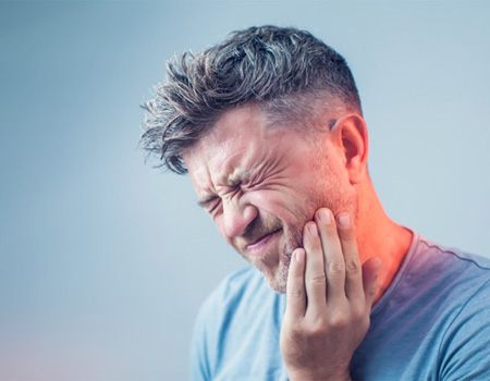 man with toothache holding the side of his jaw in pain 