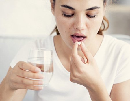 woman taking a pill with a glass of water   