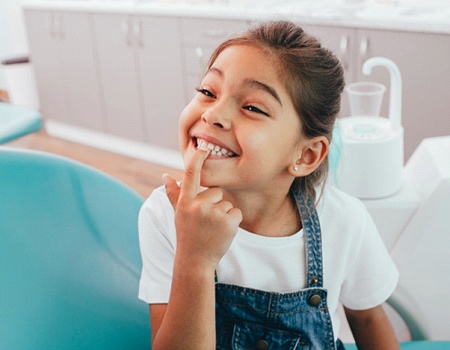 Little girl smiling and pointing to teeth after fluoride treatment