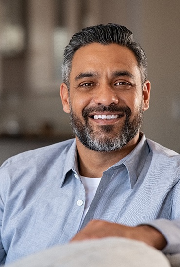 Man smiling and leaning on couch after successful dental implant salvage in Baltimore, MD