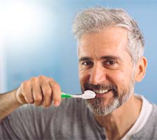Man brushing his dental implants in Azle and smiling