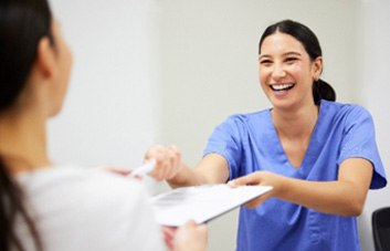 Smiling dental assistant handing patient forms