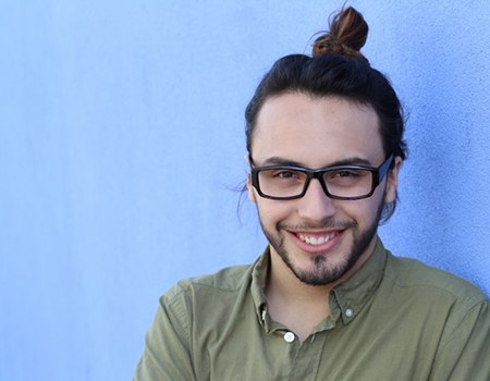 young man wearing green shirt smiling in front of blue wall 