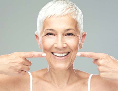 Woman pointing at her smile after teeth whitening in Azle