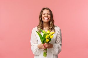 a woman smiling with a clean smile and spring flowers in her hand
